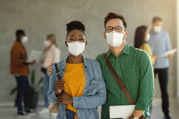 Portrait of happy college couple with protective face masks. Happy university couple with protective face masks standing in a hallway and looking at camera. kn95 face mask photos stock pictures, royalty-free photos & images