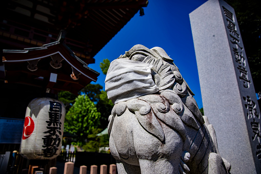 A statue of Guardian dog wearing mask at Meguro fudo temple in Tokyo. Meguro district Tokyo Japan - 08.20.2020 It is called Komainu.