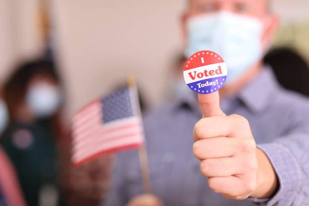istock Man votes in USA election wearing mask and I Voted sticker. 1268513558