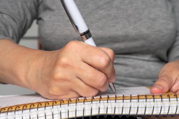 istock Woman hand is writing with white pen on spiral notebook. Selective focus. 1268515006