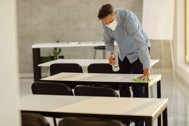 Male professor with face mask disinfecting tables after a class in lecture hall.