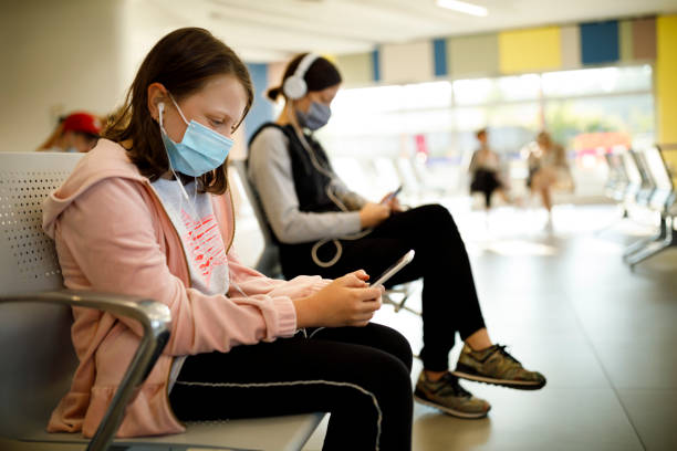 istock Kids with face protective mask using mobile phone while waiting at airport 1268534739