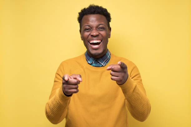 istock Handsome african man in yellow sweater pointing at camera on joke. 1268537481