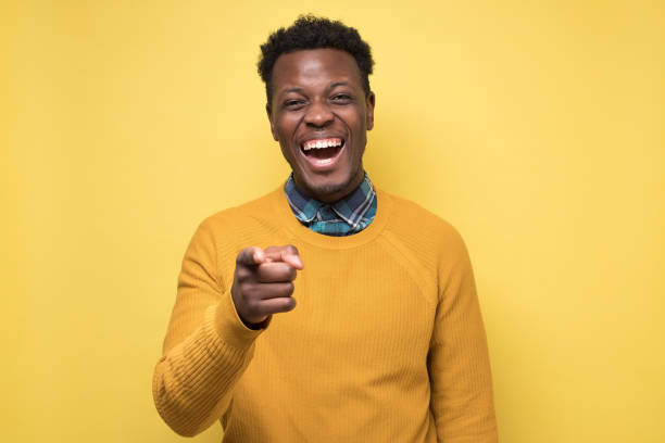 istock Handsome african man in yellow sweater pointing at camera on joke. 1268538036