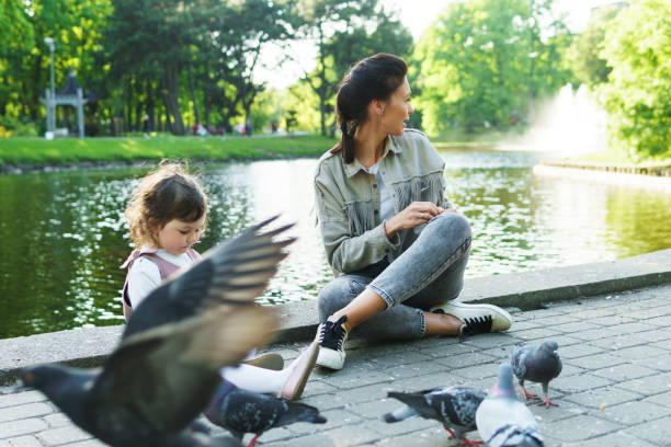 Mother and her little daughter feeding birds in city park Young mother and her cute little daughter feeding birds in city park pigeon family stock pictures, royalty-free photos & images