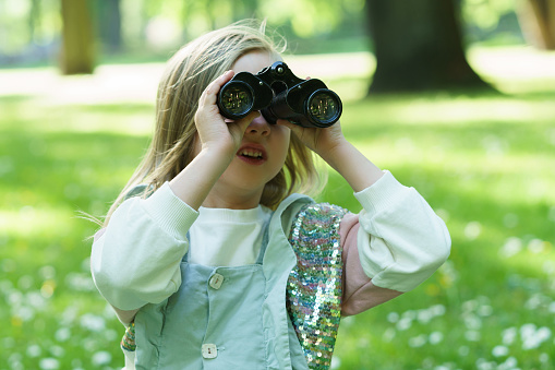 Portrait of a cute little girl with a retro binoculars in a city park