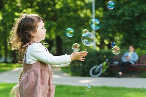Cute little girl catching soap bubbles in a city park