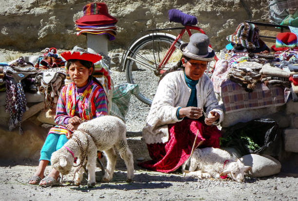Chivay, Peru - 07/22/2006: Girl wearing traditional clothes with baby sheep, mother spinning thread en selling knitwear, hats and souvenirs to tourists at the side of the road