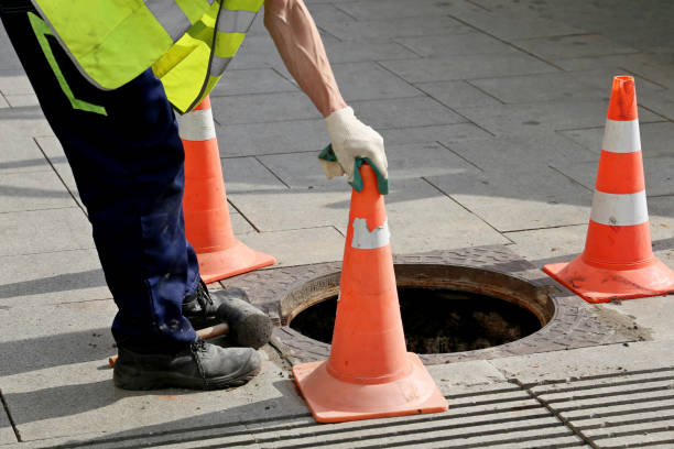 operaio sopra il portello della fogna aperta su una strada vicino ai coni del traffico - road street thoroughfare hole foto e immagini stock