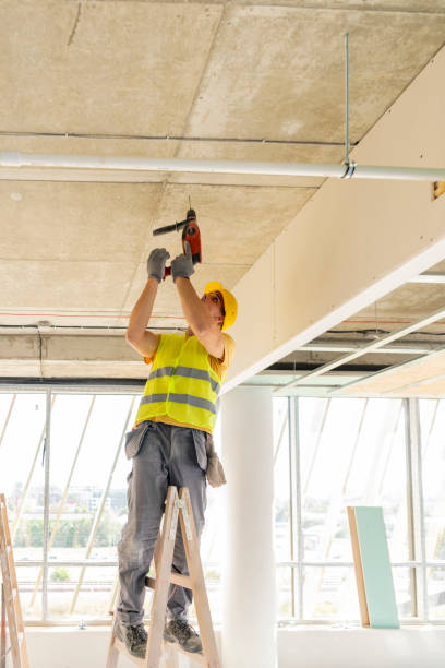 istock Young male construction worker in yellow hardhat drilling the wall with electric drill tool. Close-up front portrait with copy space 1268558849