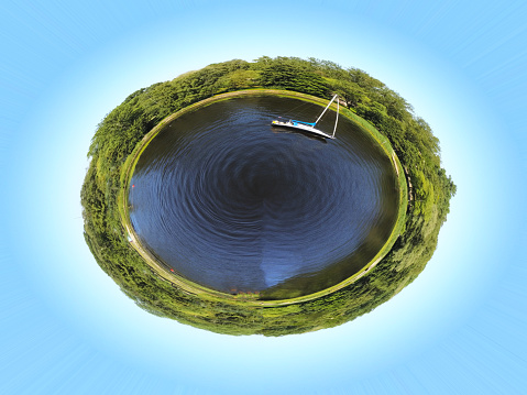 Small planet transformation of a spherical 360 degree panorama. Spherical abstract aerial view of a round lake with a boat on the water. Green trees around the lake. Curvature of space.