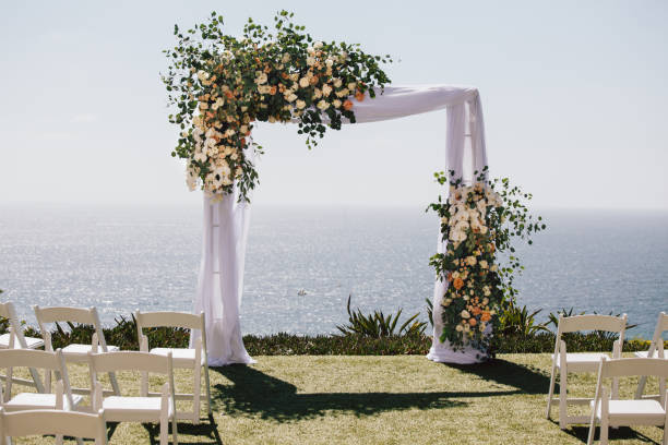 Outdoor beach ceremony area with ocean view, white chairs, floral arch on sunny day Outdoor beach ceremony area with ocean view, white chairs, floral arch on sunny day laguna niguel photos stock pictures, royalty-free photos & images