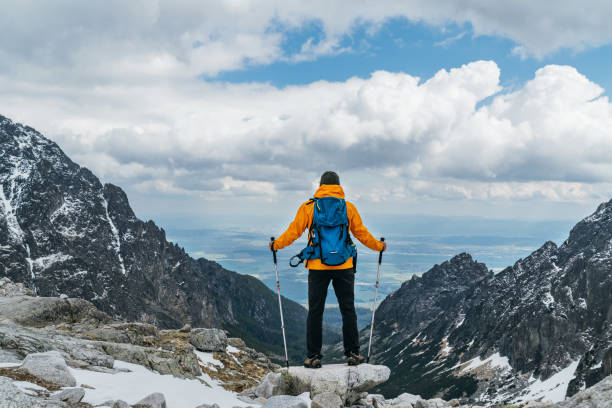 istock Dressed bright orange jacket backpacker man with trekking poles enjoying the mountain valley view during mountain walk in High Tatras, Slovakia. Active people concept 1268569896