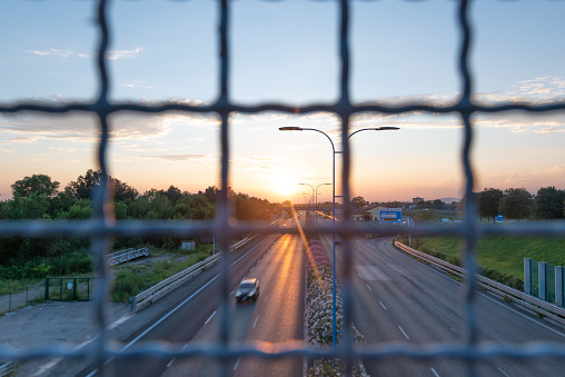 A 4K video time lapse of the highway at sunset shot from the overpass behind the road safety wire fence. Traffic flow with a wire fence in the foreground.