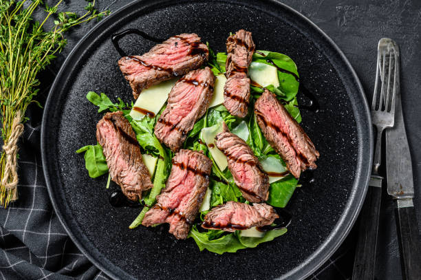 istock Steak salad with spinach, arugula and sliced beef marbled steak. Black background. Top view 1268584361