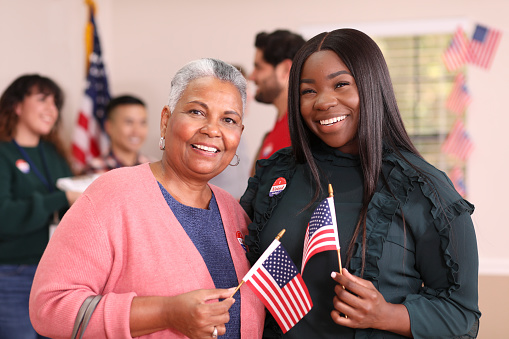 African descent mother, daughter or friends vote in the USA election.  They stand together holding flags and wearing 