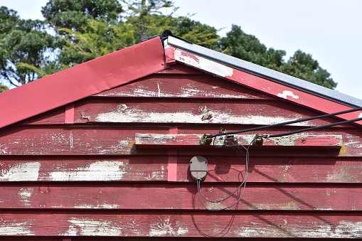 Electric wires connecting weathered wooden shed painted red to power grid.