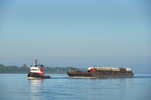 A tugboat towing tankers on a rail barge up the Fraser River. Richmond, British Columbia, Canada.