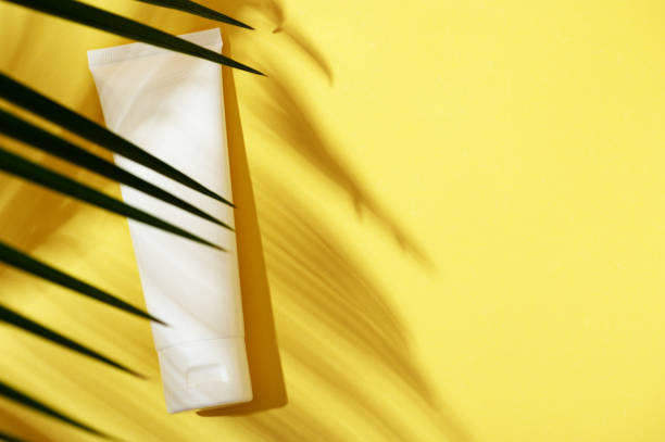 istock Packaging white plastic tube for hand cream, face, body, toothpaste top view on a yellow bright background with a shadow of a palm tree. Summer beauty skin care concept. Flat lay, copy space 1268593026