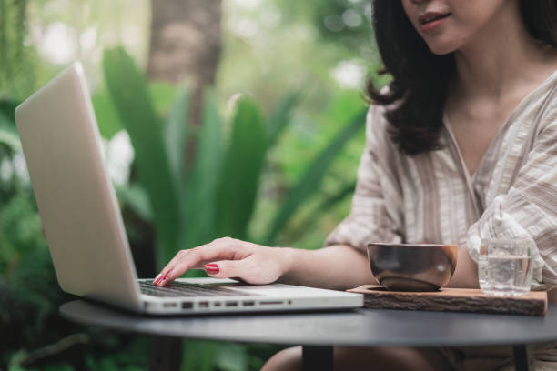istock Close up hands of woman using laptop computer working and searching online information with a cup on table in a garden.  Technology business and social distancing concept 1268602500