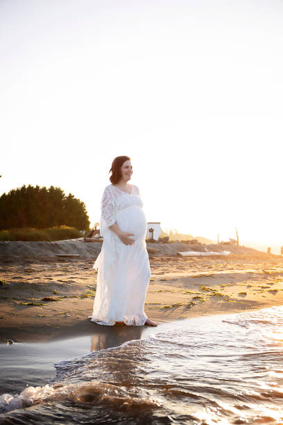 istock Pregnant woman standing on beach 1268606196