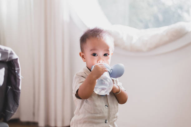 adorável menino asiático bebendo água da garrafa em casa - water child bottle little boys - fotografias e filmes do acervo