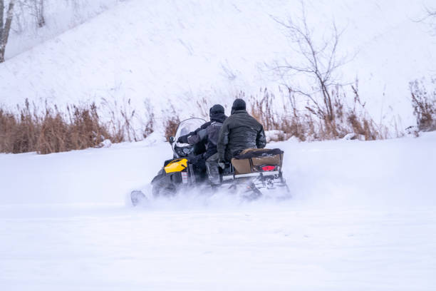 zwei mann auf einem schneemobil auf der schneefläche im winterwald - schneemobilfahren stock-fotos und bilder