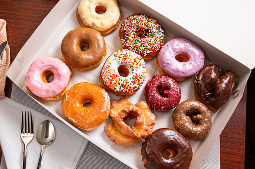 A top down view of a dozen assorted donuts in a box, in a restaurant or kitchen setting.