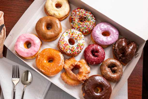 dozen donuts TD A top down view of a dozen assorted donuts in a box, in a restaurant or kitchen setting. donut stock pictures, royalty-free photos & images