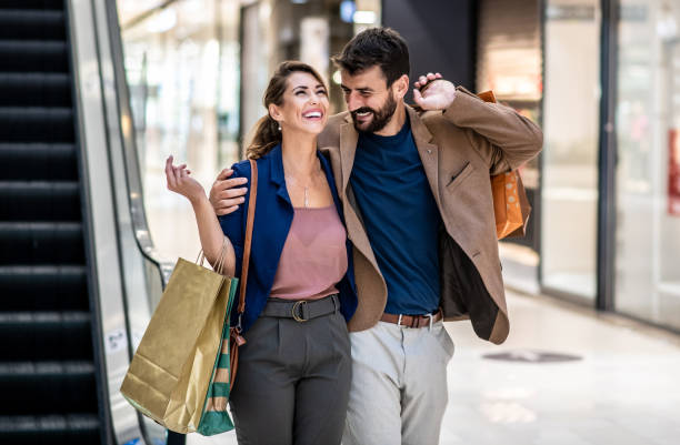 A young couple goes down the stairs in a shopping mall, carrying shopping bags and talks stock photo