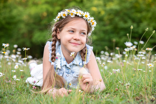 A small beautiful blonde girl in a blue linen sundress against a background of tall grass