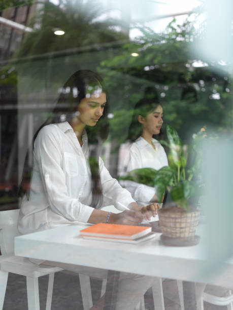 istock View through glass window of two female students concentrating on digital tablet 1268639989