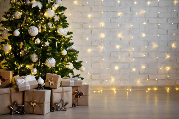 christmas tree and heap of gift boxes - copy space over white brick wall with lights stock photo