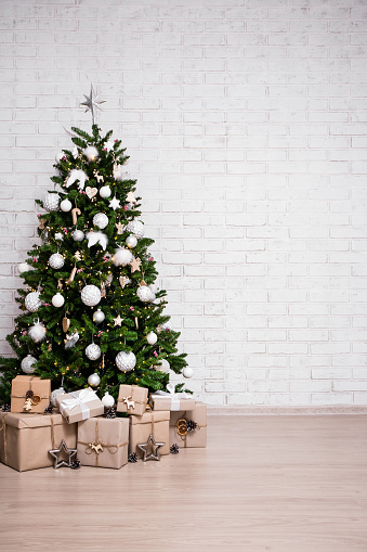 christmas and new year background - decorated christmas tree and gift boxes over white brick wall with copy space