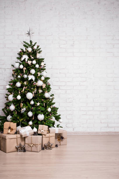 christmas and new year background - christmas tree and gift boxes over white brick wall with copy space stock photo