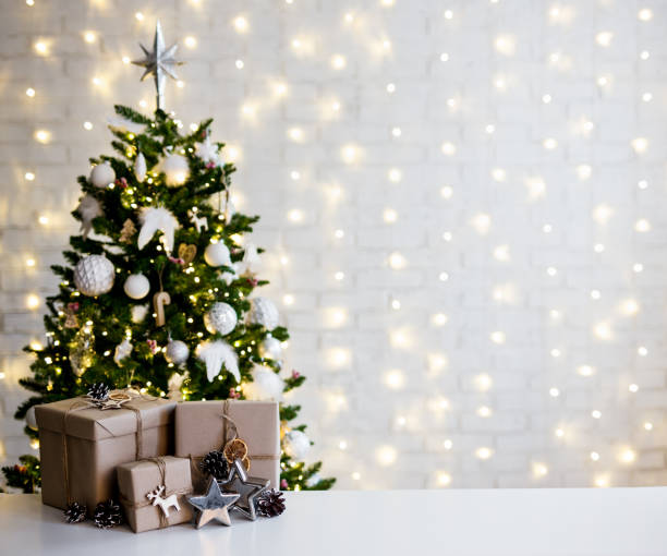 christmas and new year concept - beige gift boxes near decorated christmas tree and copy space over white brick wall stock photo