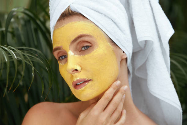 güzellik maskesi. spa prosedüründe banyo havlusu kadın portre kadar yakın. yüz yağ derma için sarı cilt bakım ürünü ile kaplı. tropical resort'ta anti-aging terapisi. - zerdeçal stok fotoğraflar ve resimler