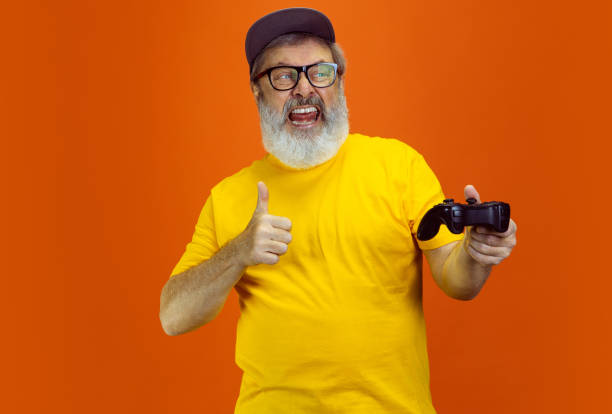 istock Senior hipster man using devices, gadgets on orange background. Tech and joyful elderly lifestyle concept 1268650689