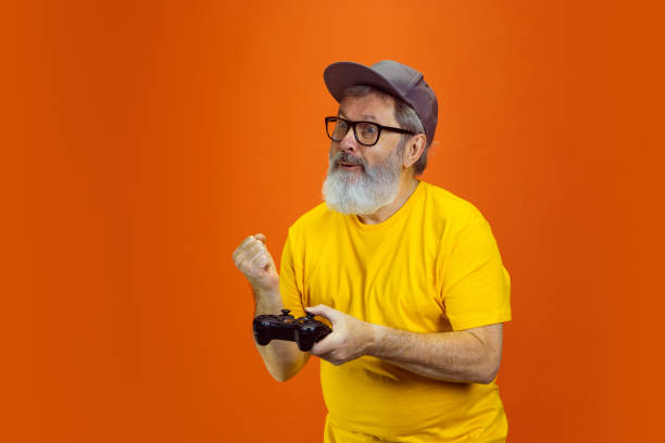 istock Senior hipster man using devices, gadgets on orange background. Tech and joyful elderly lifestyle concept 1268650691