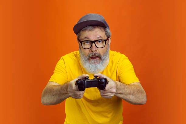istock Senior hipster man using devices, gadgets on orange background. Tech and joyful elderly lifestyle concept 1268650692