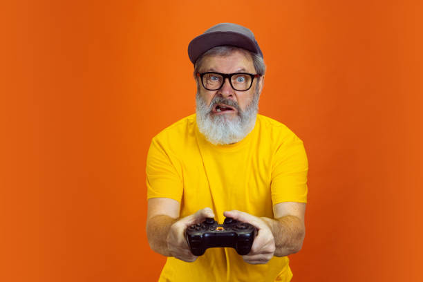 istock Senior hipster man using devices, gadgets on orange background. Tech and joyful elderly lifestyle concept 1268650698