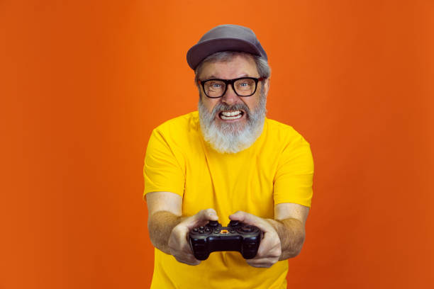 istock Senior hipster man using devices, gadgets on orange background. Tech and joyful elderly lifestyle concept 1268650703