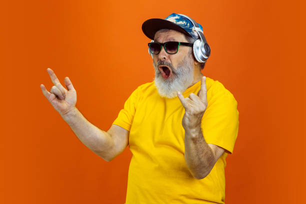 istock Senior hipster man using devices, gadgets on orange background. Tech and joyful elderly lifestyle concept 1268650706