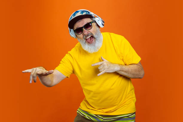 istock Senior hipster man using devices, gadgets on orange background. Tech and joyful elderly lifestyle concept 1268650707