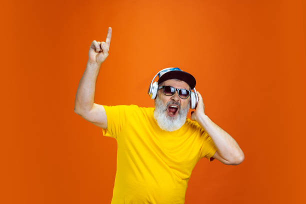 istock Senior hipster man using devices, gadgets on orange background. Tech and joyful elderly lifestyle concept 1268650718