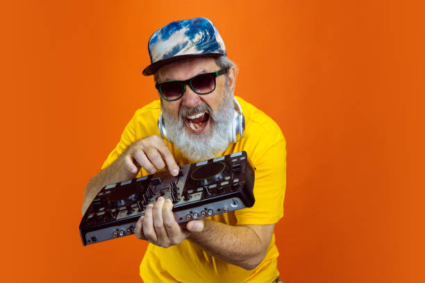 istock Senior hipster man using devices, gadgets on orange background. Tech and joyful elderly lifestyle concept 1268650723