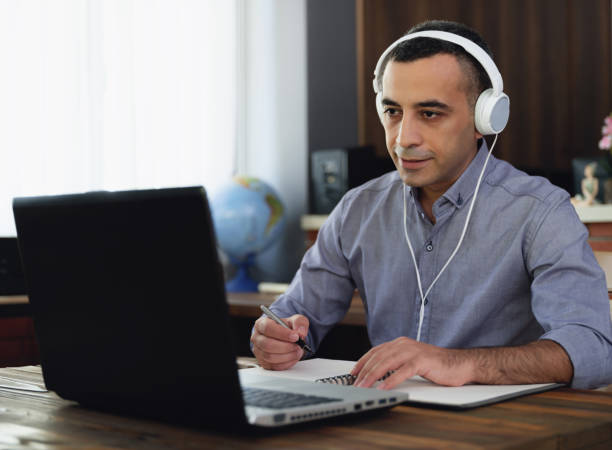 istock Man Is Working Online In Home Office Using His Laptop Computer, Joining Webinar And Taking Notes On Digital Tablet 1268650732