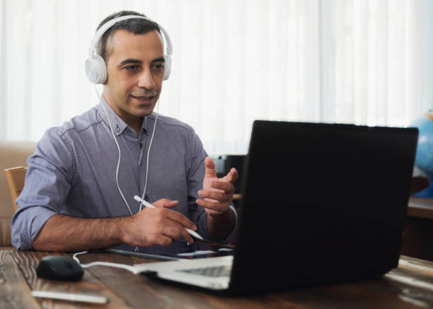 istock Man Is Working Online In Home Office Using His Laptop Computer, Joining Webinar And Taking Notes On Digital Tablet 1268651451