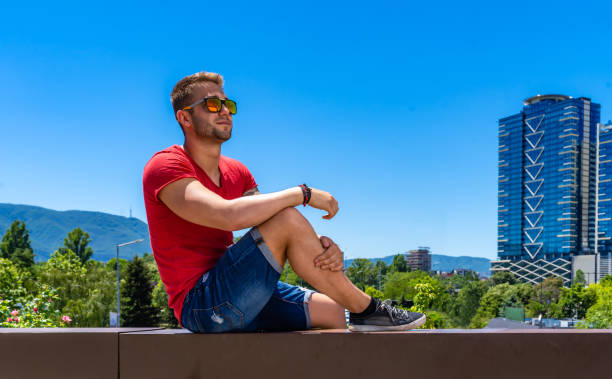istock Young man with sunglasses in front skyscraper and clear blue sky 1268652514