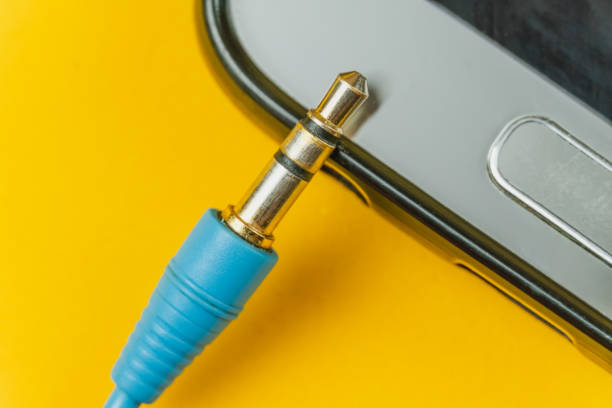 collegare da cuffie blu vicino al foro nel telefono cellulare su uno sfondo giallo, foto macro - mobile phone charging power plug adapter foto e immagini stock